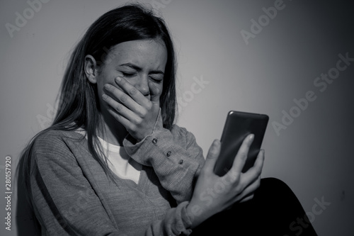 Depressed teenager girl on mobile phone victim of cyberbullying feeling sad, unhappy and lonely photo