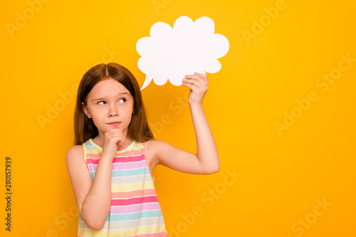 Portrait of minded child holding paper card bubble touching chin planning isolated over yellow background