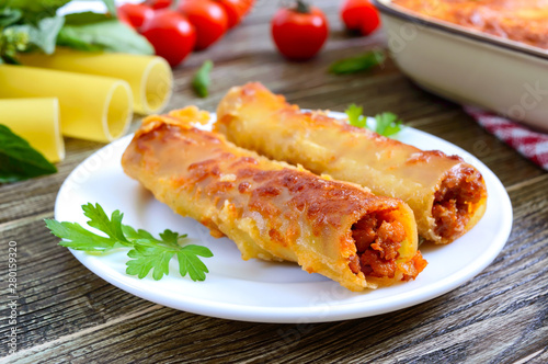 Stuffed cannelloni with bechamel sauce. Cannelloni pasta baked with meat, cream sauce, cheese on a wooden background.
