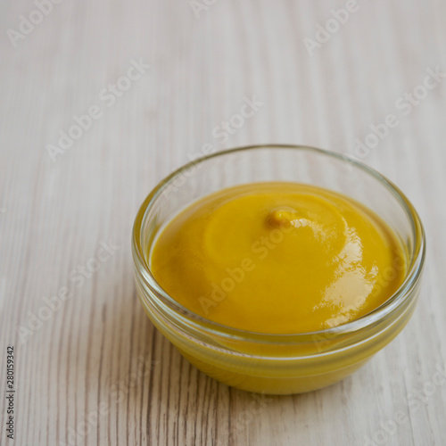 Homemade organic mustard in a glass bowl on a white wooden surface, low angle view. Close-up.