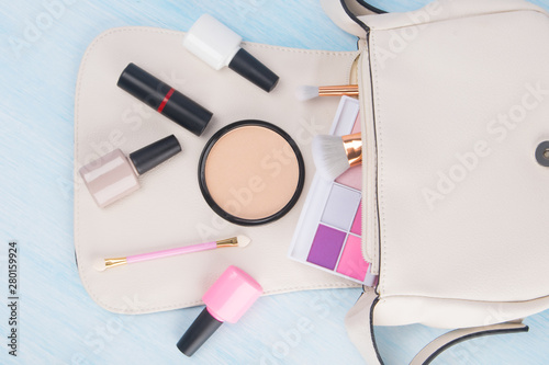 on a light background, from a white cosmetic bag, scattered items for manicure and makeup, colored eyeshadow, brushes , face powder, nail Polish and red lipstic
