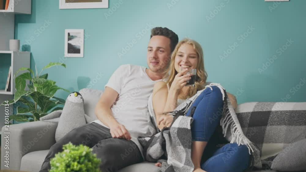Young couple drinking coffee and watching tv on the couch Young couple drinking coffee and watching tv on the couch