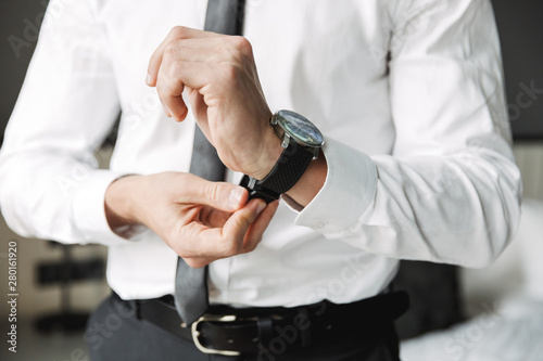 Cropped image of confident young man taking off his wristwatch in hotel room during business trip