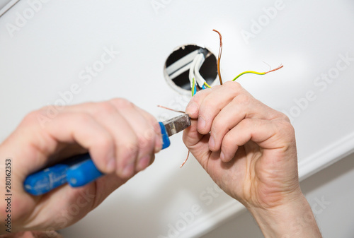 Man is holding pliers in his hands. Electrical insulator for light bulb. Adhesive tape for maintenance repair works in the flat. Restoration indoors.