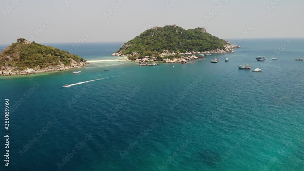 Boats and pier near small islands. Motor dive boats floating on calm blue sea near unique small islets connected with beaches and pier on sunny day in Thailand. Nang yuan koh tao