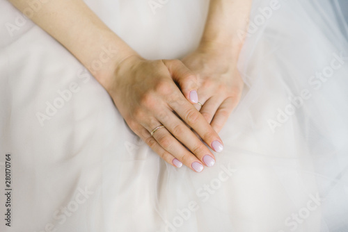 the bride's hands are folded and lie on the wedding dress, wedding manicure and wedding ring on the finger