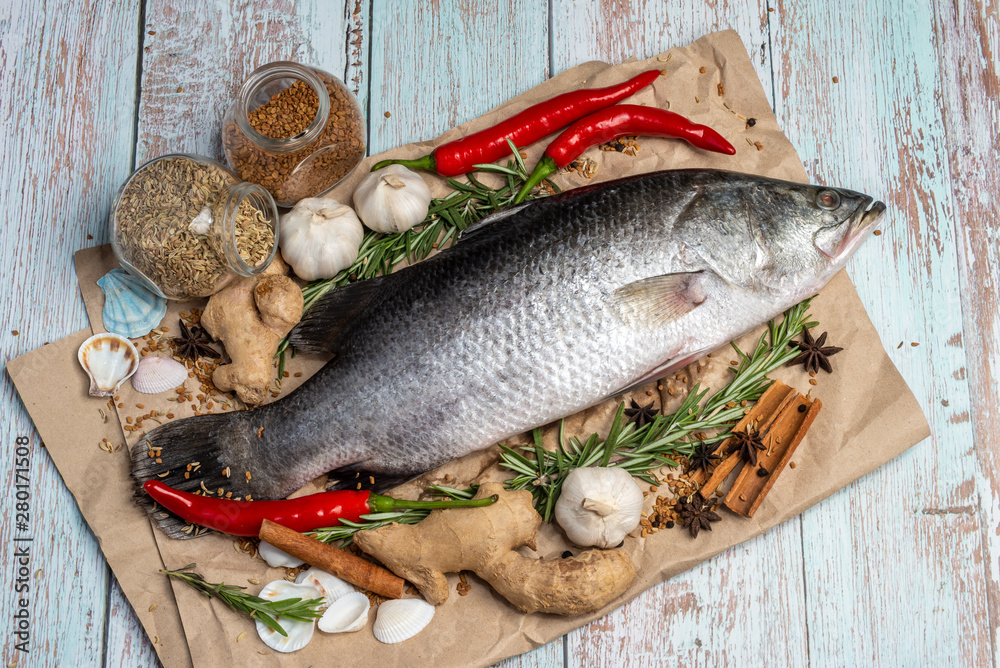 Fresh Raw Sea Bass on wooden table surrounded by fresh ingredients and spices. Fresh Raw Sea Bass on wooden table surrounded by fresh ingredients and spices.