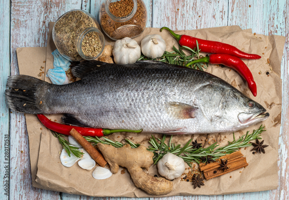Fresh Raw Sea Bass on wooden table surrounded by fresh ingredients and spices. Fresh Raw Sea Bass on wooden table surrounded by fresh ingredients and spices.