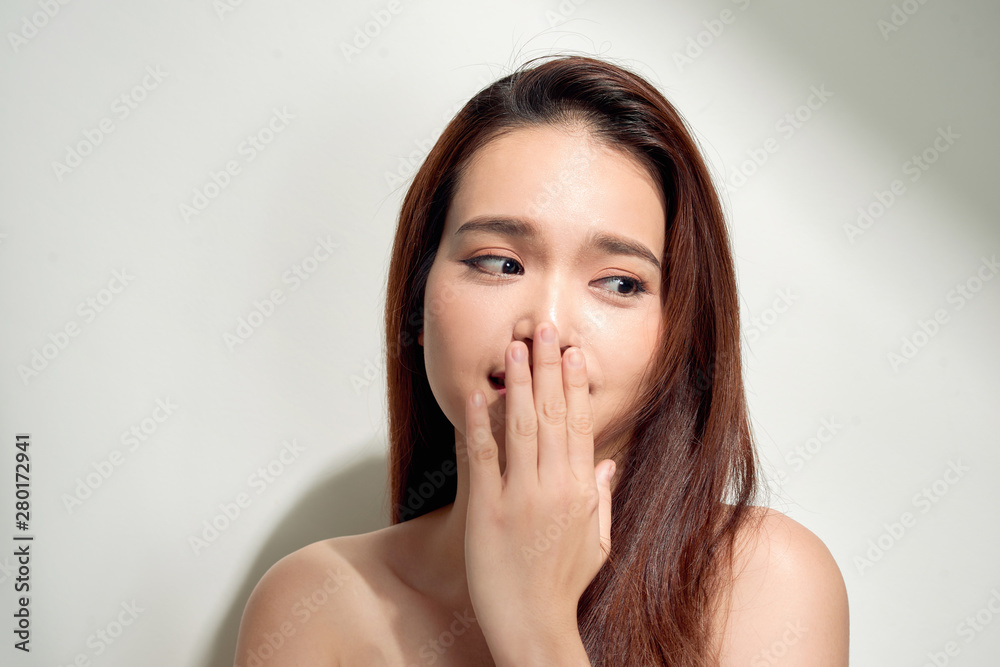 Portrait of a young beautiful girl with long hair wearing pink cotton blouse, standing looking shy hiding behind her hand and smiling, on a white background Portrait of a young beautiful girl with long hair wearing pink cotton blouse, standing looking shy hiding behind her hand and smiling, on a white background