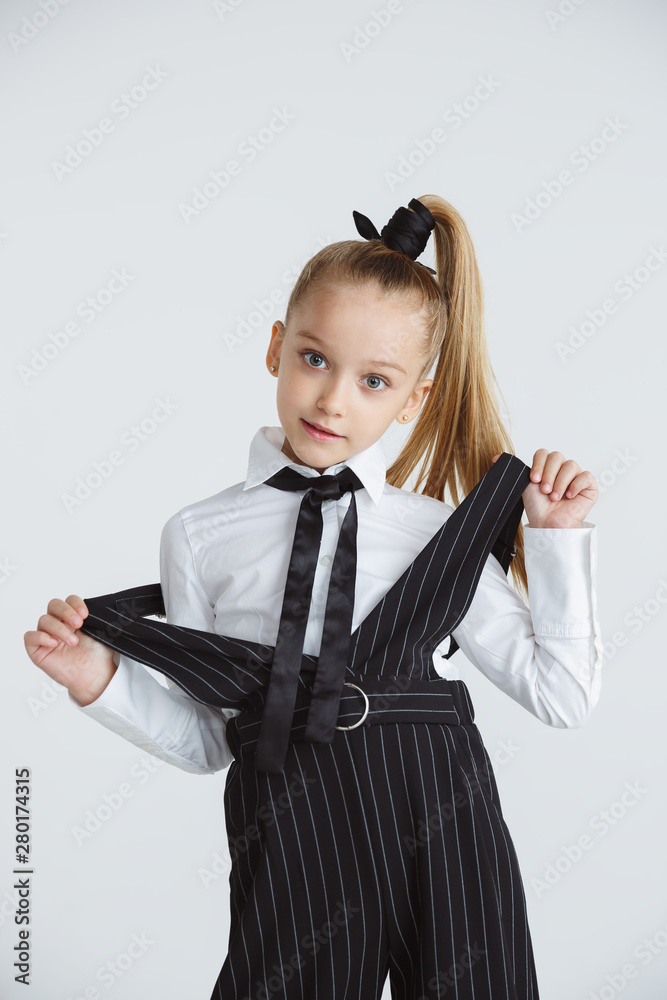 Girl preparing for school after a long summer break. Back to school. Little female caucasian model posing in school's uniform on white studio background. Childhood, education, holidays concept. Girl preparing for school after a long summer break. Back to school. Little female caucasian model posing in school's uniform on white studio background. Childhood, education, holidays concept.