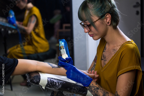 Tattoo artist demonstrates the process of getting black tattoo with paint. Master works in blue sterile gloves. Master of tattoo fill circuit tattoo.