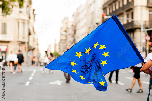  young person walks in the streets in daylight holding european union flag with blood stains on it protesting against immigration policies