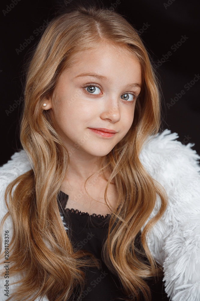 Stylish little smiling girl posing in white outfit isolated on black studio background. Beautiful caucasian blonde female model's posing. Human emotions, facial expression, childhood, fashion, style. Stylish little smiling girl posing in white outfit isolated on black studio background. Beautiful caucasian blonde female model's posing. Human emotions, facial expression, childhood, fashion, style.