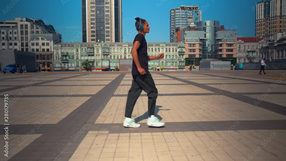 side view young man listening music via headphones walking on the street summer season