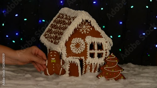 The hand-made eatable gingerbread house, adding by hand of little man, New Year tree, snow decoration, garland background illumination