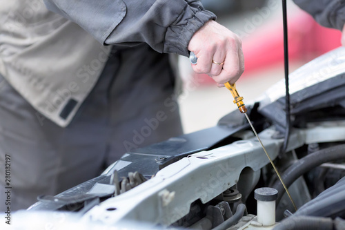 Car repair service. Mechanic checking the oil level in car engine.