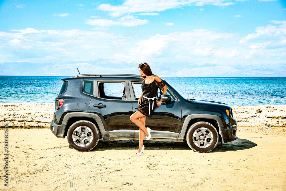 A young woman on a black car and beautiful sandy beach and blue ocean background.