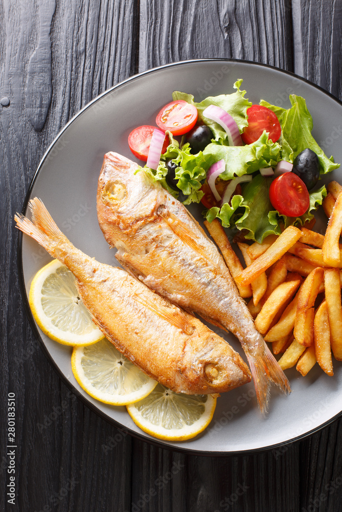 Fried pink dorado fish served with french fries and vegetable salad close-up on a plate. Vertical top view Fried pink dorado fish served with french fries and vegetable salad close-up on a plate. Vertical top view
