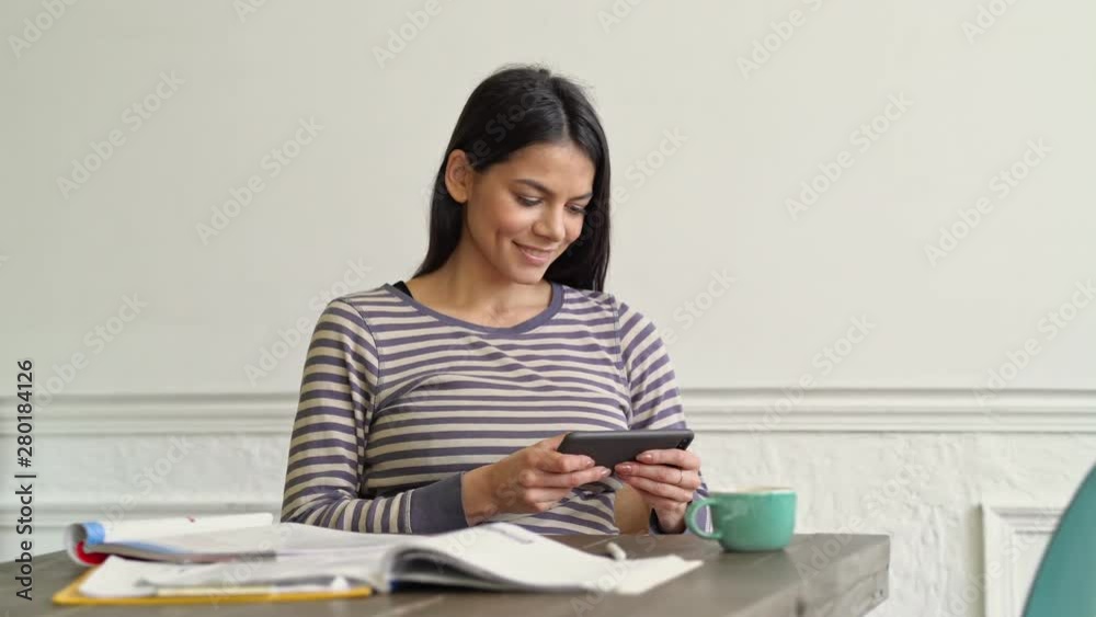 Beautiful young woman playing game on the smatphone sitting at the table Beautiful young woman playing game on the smatphone sitting at the table