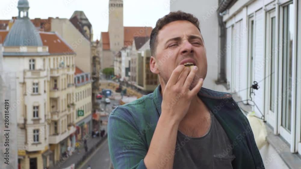 Man eating a hamburger on a hotel balcony in a big city Man eating a hamburger on a hotel balcony in a big city