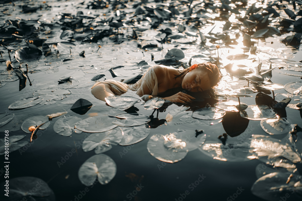 Young woman lying in the water among the leaves and flowers of yellow ...