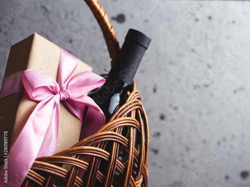 A bottle of red wine and a gift box with a bow in a basket with copyspace photo