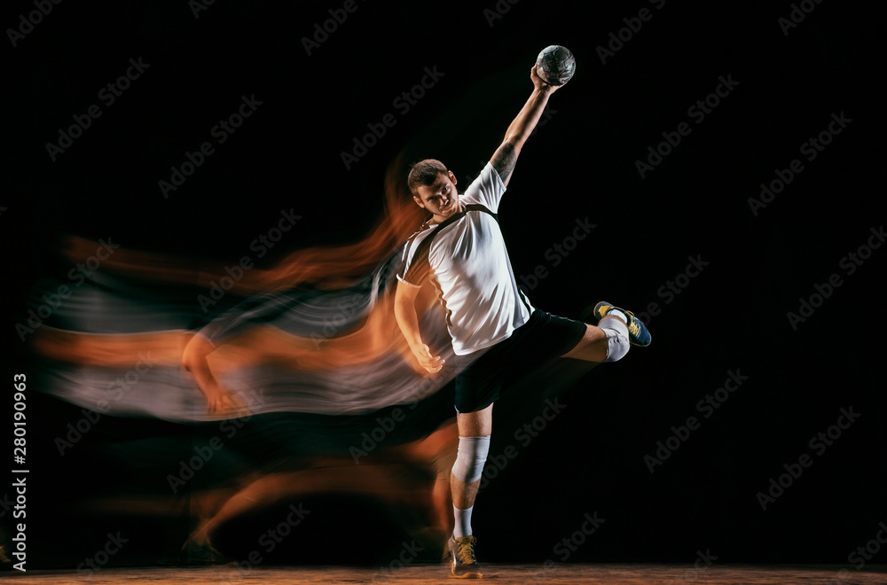 Obraz premium Caucasian young handball player in action and motion in mixed lights over black studio background. Fit male professional sportsman. Concept of sport, movement, energy, dynamic, healthy lifestyle.