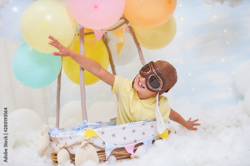 A little boy sits in a balloon basket in the clouds, pretending to travel  and fly with an Aviator hat for a concept of creativity or imagination.  Stock Photo | Adobe Stock
