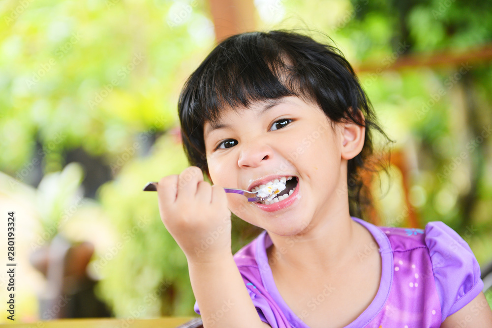 Cute little girl eating cake - Asian child happy and holding a spoon into the mouth with cake on dining table , selective focus Cute little girl eating cake - Asian child happy and holding a spoon into the mouth with cake on dining table , selective focus