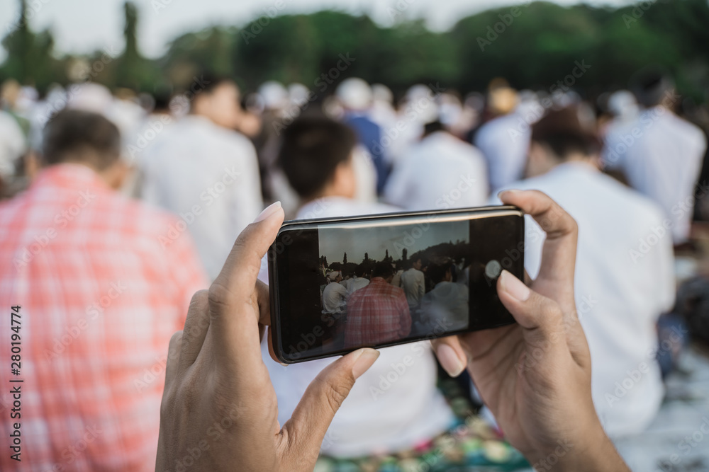Hands holding cellphone and captures the moment of Eid prayer with a cellphone camera
