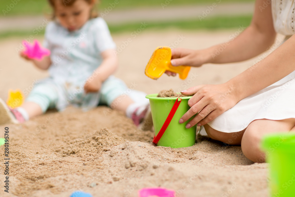 childhood, leisure and people concept - close up of mother with sand in toy bucket playing with little baby daughter in sandbox childhood, leisure and people concept - close up of mother with sand in toy bucket playing with little baby daughter in sandbox