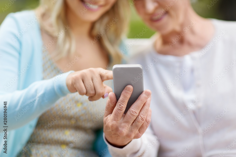 family, generation and people concept - close up of happy smiling adult daughter and senior mother with smartphone sitting on park bench family, generation and people concept - close up of happy smiling adult daughter and senior mother with smartphone sitting on park bench