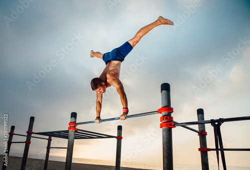 fitness, sport, training, calisthenics and lifestyle concept - young man exercising handstand on bar outdoors photo