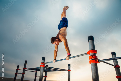 fitness, sport, training, calisthenics and lifestyle concept -  young man exercising olympic handstand on bar outdoors