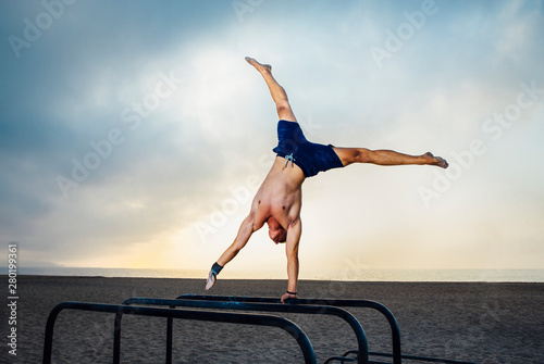 fitness, sport, training, calisthenics and lifestyle concept -  young man exercising one arm handstand on bar outdoors