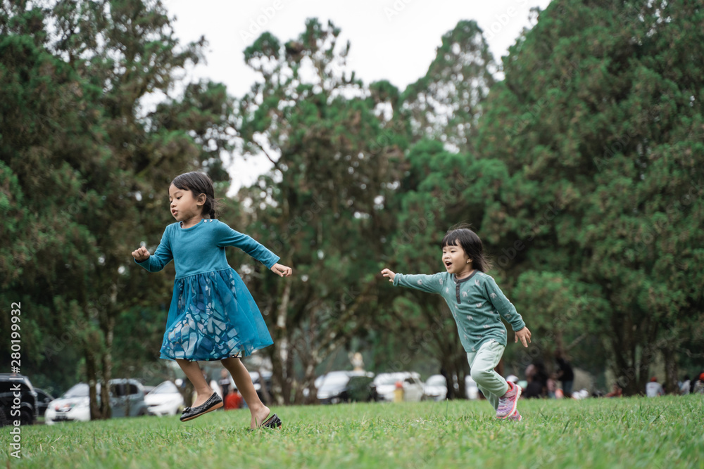 two little girls playing chase each other when enjoy playing together in the park