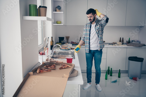 Portrait of his he nice attractive minded pensive unsure bearded guy wearing checked shirt mess chaos around maid order service in modern light white interior style kitchen indoors