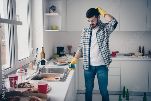 Portrait of his he nice attractive minded annoyed bearded guy wearing checked shirt mess chaos around maid service in modern light white interior style kitchen indoors