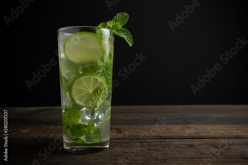 Mojito drink with lime, lemon and mint on wooden table.