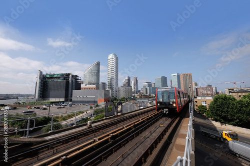 London  United Kingdom 6th July 2019  Canary Wharf skyline seen from Tower Hamlets  DLR Docklands Light Railway train in foreground on summer day  logos removed