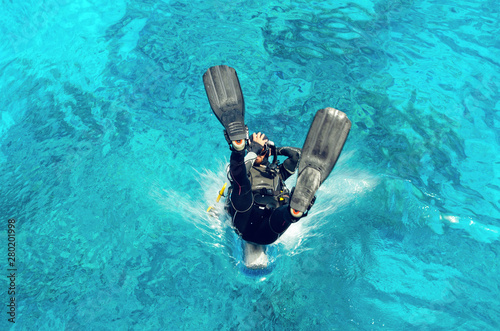 Diver in a wetsuit and flippers jumping in the blue water.