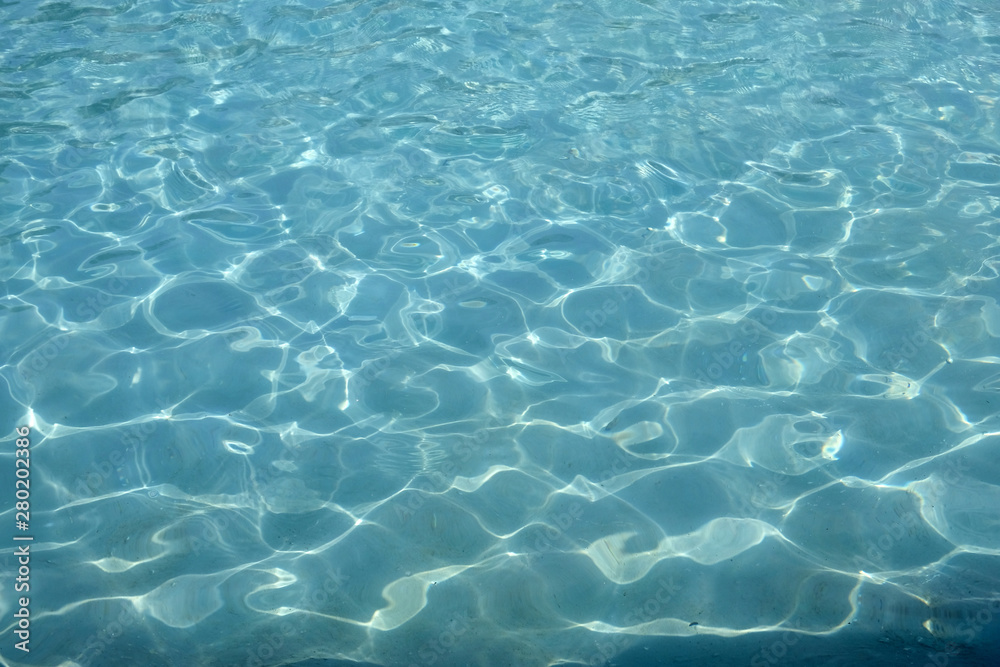 Blue water in the pool background. Water surface with a reflection of sun glare texture.