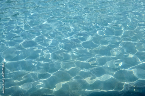 Blue water in the pool background. Water surface with a reflection of sun glare texture.