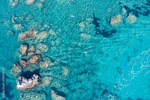 Aerial view of turquoise sea water and rocks by the seashore.