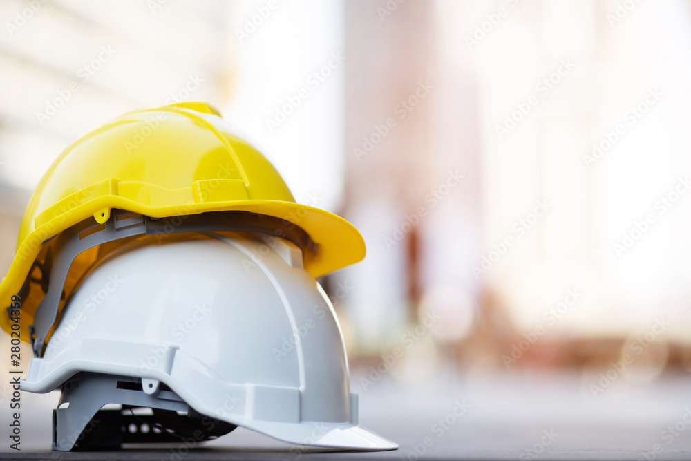 yellow and white hard safety wear helmet hat in the project at construction site building on concrete floor on city with sunlight. helmet for workman as engineer or worker. concept safety first.  - obrazy, fototapety, plakaty 