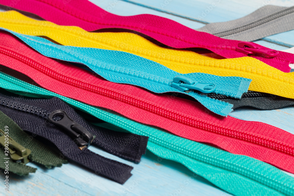 Pack a lot of colorful plastic zippers stripes with sliders pattern for handmade sewing tailoring on the blue denim background close up selective focus Pack a lot of colorful plastic zippers stripes with sliders pattern for handmade sewing tailoring on the blue denim background close up selective focus
