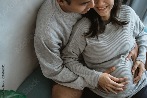happiness husband and wife feel pregnancy, sit back together on the couch while holding the belly of a pregnant wife