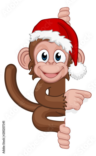 A Christmas monkey animal cartoon character in a Santa hat behind a sign peeking around and pointing at it photo