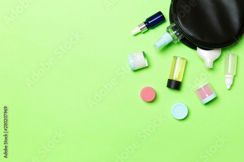 Group of beauty cream bottles dropped out of the cosmetics bag on green background. Space for your design. Top view of skincare concept