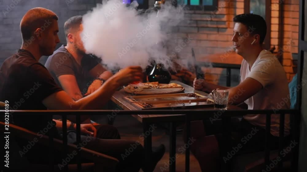 Men friends smoking hookah playing backgammon in a bar Men friends smoking hookah playing backgammon in a bar